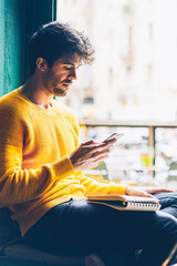 Pensive bearded man dressed in casual outfit checking email and reading notification on modern...