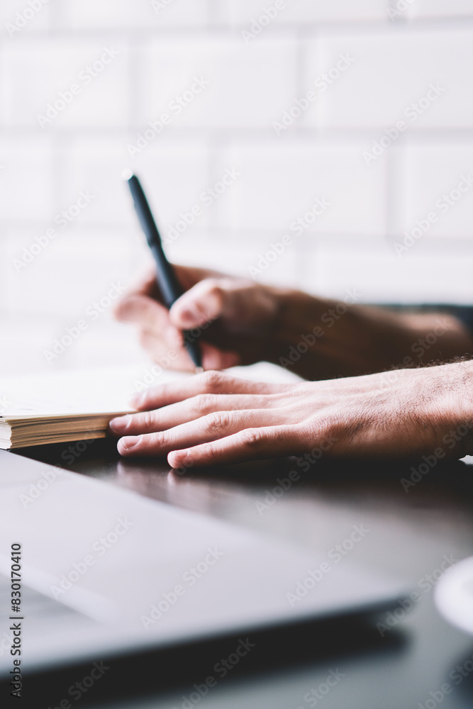 Poster cropped image of businessman dressed in black shirt writing down text information in notepad while w