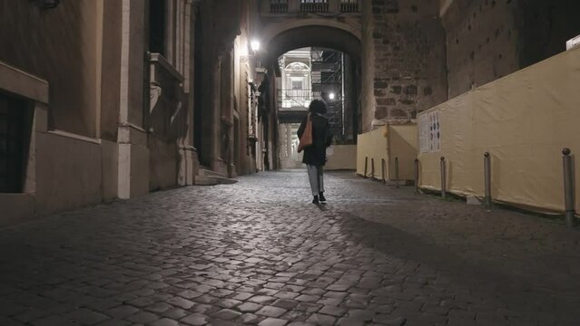Stylish business woman walk on cobblestone passage street at Capitoline square in Rome, Italy at night, slow motion