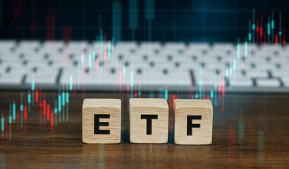 Exchange traded fund, ETF concept on wooden cubes with keyboard of computer and blurred stock market trading graphs with candlestick charts on wooden table background. Financial market concept.