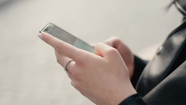 Close-up view of hands holding a smartphone, focusing on messaging and communication. A person is using a phone wearing a stylish ring and leather jacket. Hands Using Smartphone for Messaging