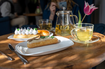 A cozy cafÃ© scene features a wooden table adorned with pastries, a teapot, cups, and a striking pink tulip, creating an inviting atmosphere for leisurely dining and socializing