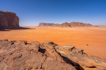 Majestic Desert Valley in Wadi Rum, Jordan: Expansive Red Sands and Towering Sandstone Cliffs Under Clear Blue Sky