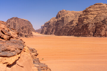 Majestic Desert Valley in Wadi Rum, Jordan: Expansive Red Sands and Towering Sandstone Cliffs Under Clear Blue Sky