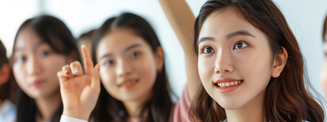 High school classmates, their expressions animated as they participate in a lesson, a smiling, confident Asian girl raising a hand to answer the teacher's query..