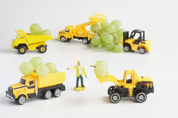 Toy machines and a worker harvest fresh grapes. White background. The concept of mechanization of agricultural work and delivery of products. Toy world. Photo. Copy space