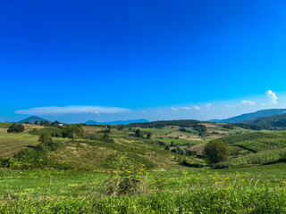 View of small hills and larger mountains with a small field and a house, Han Kola, Bosnia