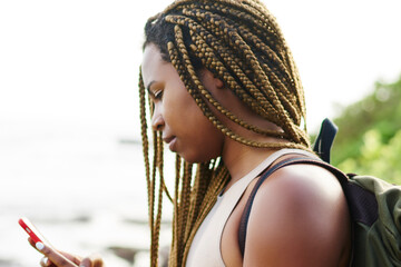 Dark skinned young tourist with dreads searching online navigator on smartphone standing...