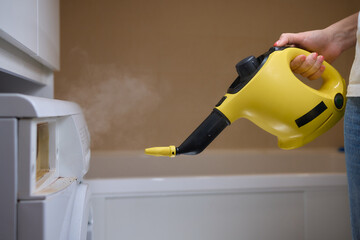 hand in gloves. Using a steam cleaner to clean a washing machine