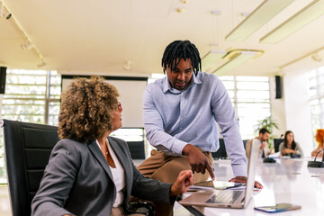 Two multiracial business colleagues working together in the office on laptops and tablets
