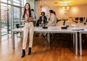 Portrait of young Hispanic businesswoman standing in front of her colleagues with tablet.