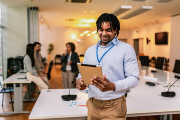 Portrait of young African American businessman standing in front of his colleagues with tablet.