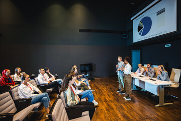 Asian and African American business people having speach on a press conference in a convention center.Diagrams on a smartboard