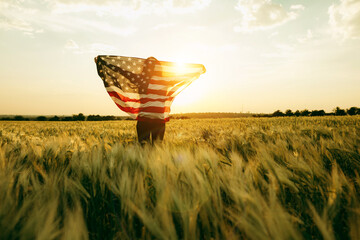 Young woman with American flag in a wheat field at sunset. 4th of July. Patriotic holiday, american...