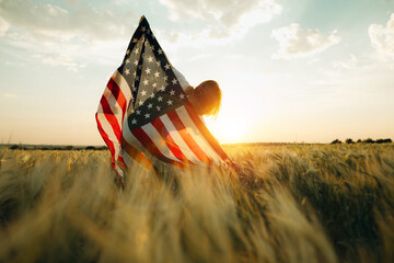 Young happy woman with American flag in a wheat field at sunset celebrate Independence day. 4th of...