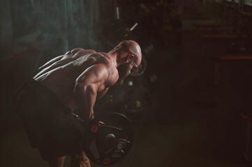 Caucasian bald topless man doing an exercise with a barbell in the gym. 