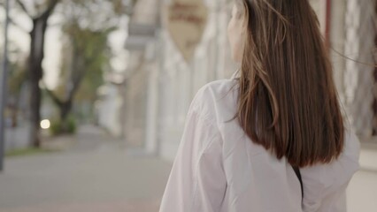 A cheerful young woman in a white blouse walking down a sunny urban street, exuding casual elegance and confidence. Smiling Young Woman Walking in a Sunny City Street