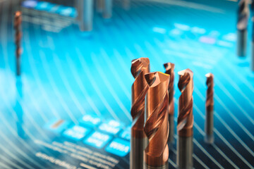 A close up of a blue background with a group of metal drill bits on it. The drill bits are all...