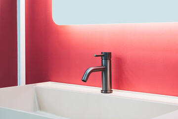 A sink with a silver faucet and a red wall behind it