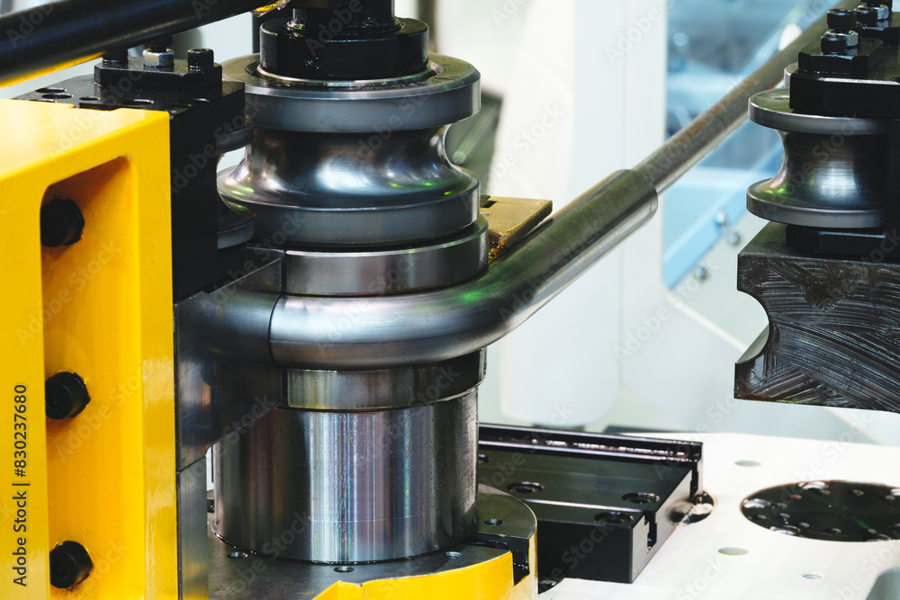 Poster a machine is bending a metal pipe. the machine is yellow and black. the pipe is bent into a curve