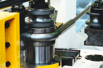 A machine is bending a metal pipe. The machine is yellow and black. The pipe is bent into a curve
