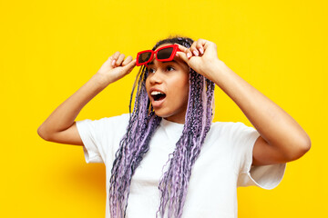 shocked african american woman in sunglasses with colored dreadlocks looking at copy space on...