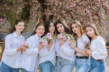 A group of young women are posing for a photo with flowers in their hands. Scene is cheerful and lighthearted, as the girls are smiling and enjoying the moment