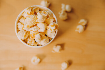 A bucket of popcorn, top-view, warm colors, light brown wooden background, flat lay, daylight macro close-up