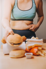 To eat or not. Cheerless plump woman looking at the burger while thinking to eat it or not