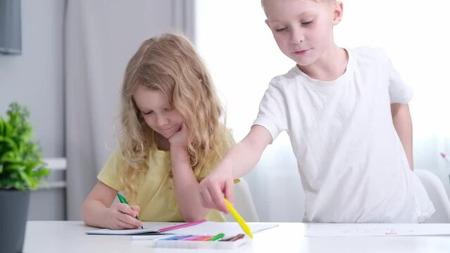 two cute blond Caucasian preschooler children draw with pencils at the table at home. children's development. family pastime
