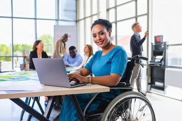 Happy, successful young disabled black female in a wheelchair, working in a tech company. in an open plan office with diverse workforce.
