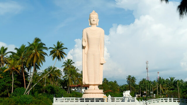Tsunami Honganji Vihara, Hikkaduwa, Sri Lanka. Action. Beautiful white statue among green palm trees and blue cloudy sky.