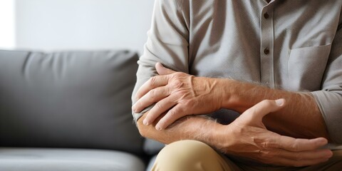 Elderly man in living room coping with hand and wrist pain due to medical conditions. Concept Elderly Care, Physical Therapy, Pain Management, Hand and Wrist Health, Medical Conditions