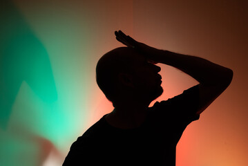 Studio portrait of a man in silhouette with his hand over his head.