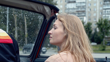 Young couple in countryside area sitting together in a car. Stock. Red flag on a back seat, retro car in a village.