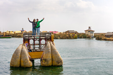A couple of people stand on a traditional reed boat with outstretched arms. Lake Titicaca. Peru