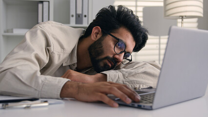 Lazy weary sleepy male manager tired exhausted Arabian Indian businessman employee working computer...