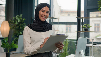 Happy muslim Islam woman Arabian girl in hijab HR manager secretary with paper tablet write notes sign data in note tablet writing to-do list business ideas successful businesswoman planning workflow