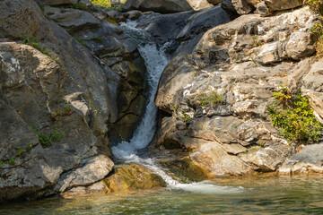 waterfall cascades between rugged rocks, its clear waters reflecting the tranquil beauty of an untouched natural landscape, inviting a moment of peaceful reflection