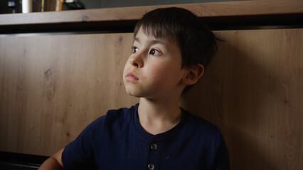 A young boy is leaning against a wooden counter, gazing upward