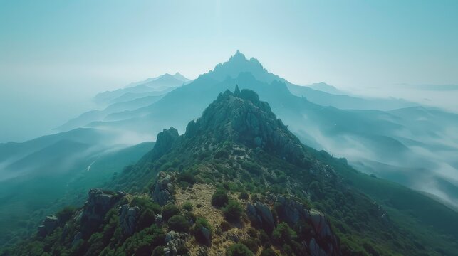 Misty mountain landscape with rugged peaks under a soft blue sky, shrouded in swirling clouds.