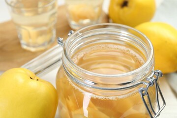 Delicious quince drink in glass jar and fresh fruits on table, closeup