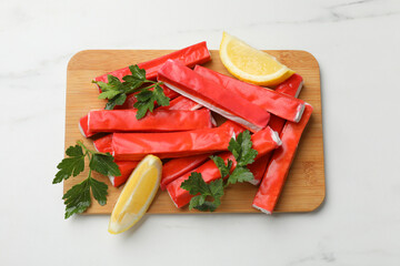 Tasty crab sticks, parsley and lemon wedges on white table, top view