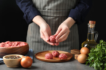 Woman making meatball from ground meat at grey table, closeup