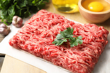 Raw ground meat and parsley on table, closeup