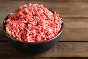 Raw ground meat in bowl on wooden table, closeup