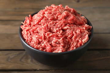 Raw ground meat in bowl on wooden table, closeup
