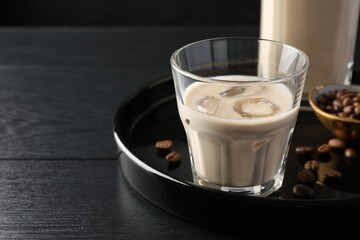 Coffee cream liqueur in glass and beans on black wooden table, space for text
