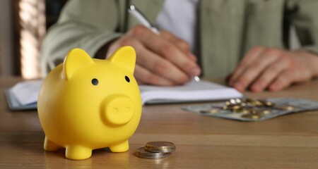 Man at wooden table, focus on yellow piggy bank. Space for text