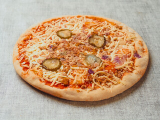 A pizza with cheese and pickles on top. Italian dish with dough, sauce and cheese. Simple white table cloth. Popular food.
